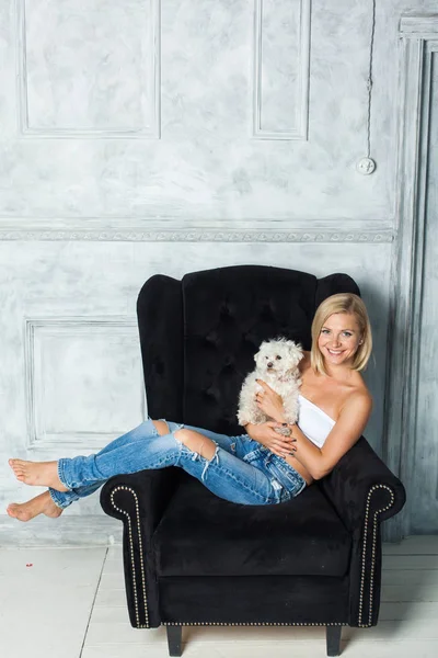 Блондинка сидить на стільці, граючи зі своїм собакою — стокове фото