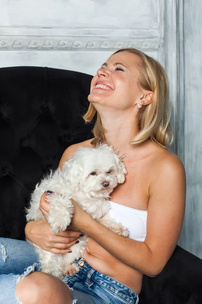 Блондинка сидить на стільці, граючи зі своїм собакою — стокове фото