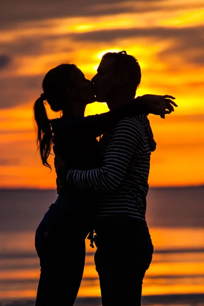 Siluetter av kvinna och man på en bakgrund av färgsprakande solnedgång av en molnig dag på stranden — Stockfoto