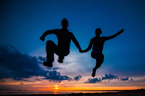 Silhuetas de mulher e homem em um fundo de pôr do sol colorido de um dia nublado na praia — Fotografia de Stock