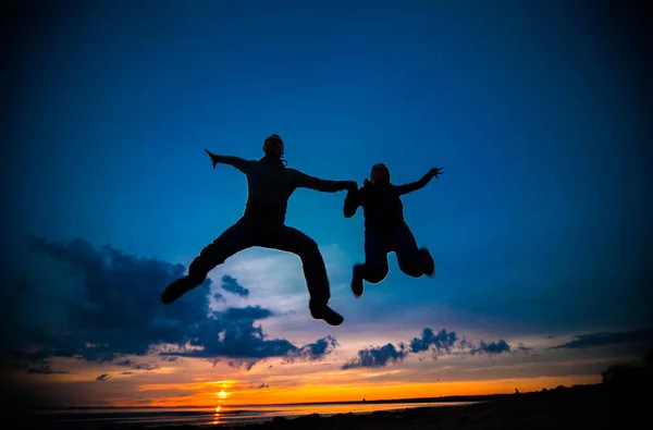 Silhuetas de mulher e homem em um fundo de pôr do sol colorido de um dia nublado na praia — Fotografia de Stock