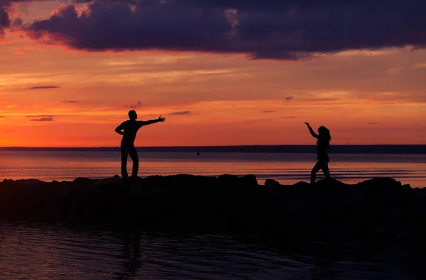 Silhuetas de mulher e homem em um fundo de pôr do sol colorido de um dia nublado na praia — Fotografia de Stock