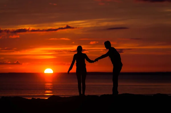 Sziluettek a nő és a férfi a háttérben a színes naplementét egy felhős nap a strandon — Stock Fotó
