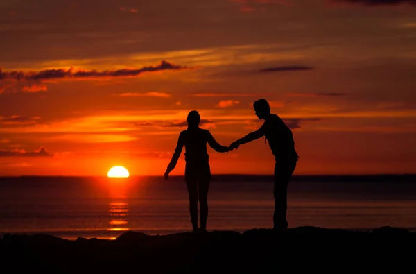 Silhouetten von Frau und Mann auf einem Hintergrund des bunten Sonnenuntergangs eines bewölkten Tages am Strand — Stockfoto