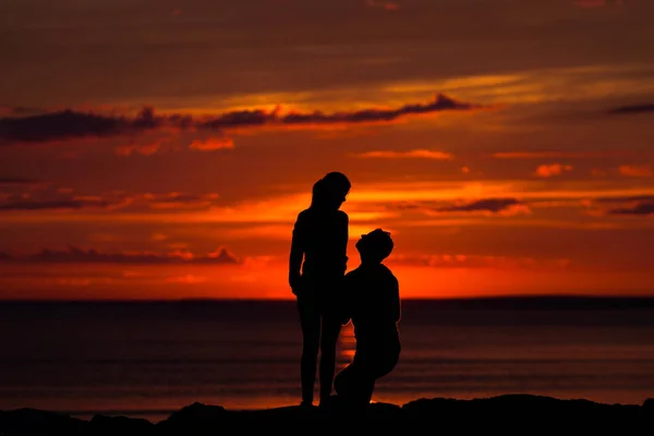 Silhuetter av kvinne og mann på en grunn av fargerik solnedgang fra en overskyet dag på stranden – stockfoto