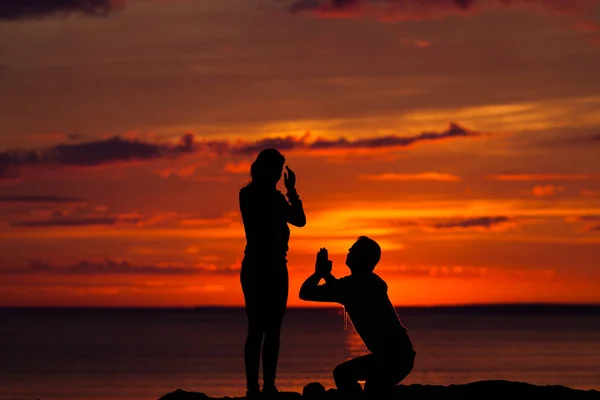 Sziluettek a nő és a férfi a háttérben a színes naplementét egy felhős nap a strandon — Stock Fotó