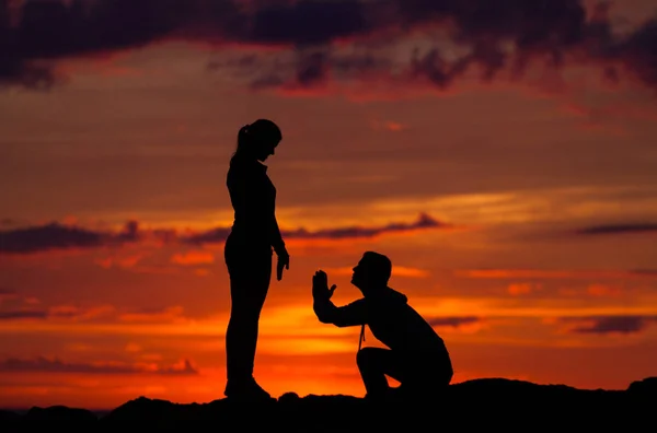 Silhuetas de mulher e homem em um fundo de pôr do sol colorido de um dia nublado na praia — Fotografia de Stock