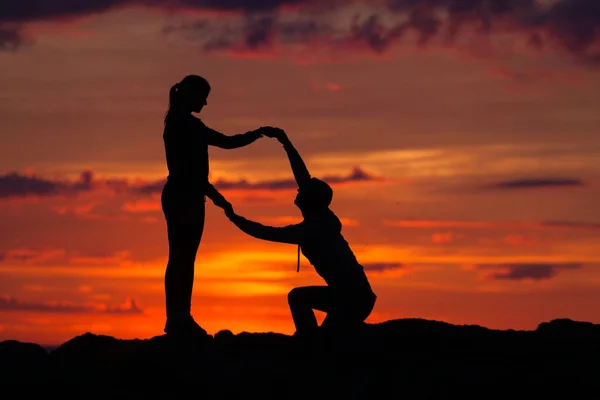 Silhuetas de mulher e homem em um fundo de pôr do sol colorido de um dia nublado na praia — Fotografia de Stock