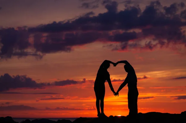 Silhuetas de mulher e homem em um fundo de pôr do sol colorido de um dia nublado na praia — Fotografia de Stock