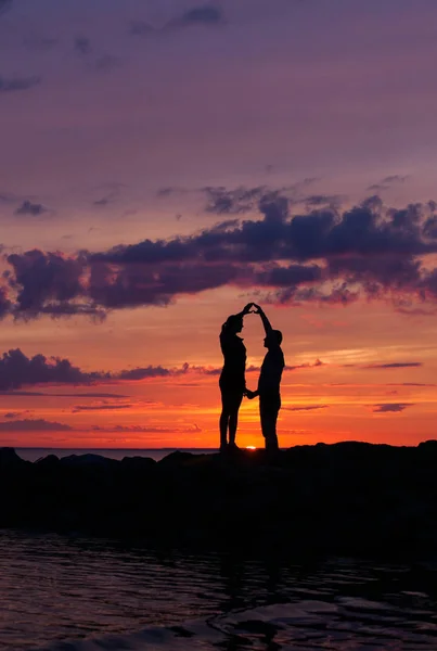 Siluetas de mujer y hombre sobre un fondo de colorido atardecer de un día nublado en la playa — Foto de Stock