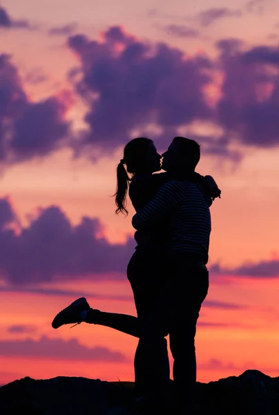 Silhouetten von Frau und Mann auf einem Hintergrund des bunten Sonnenuntergangs eines bewölkten Tages am Strand — Stockfoto