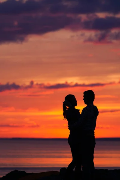 Silhouettes of woman and man on a background of colorful sunset of a cloudy day on the beach — Stock Photo, Image