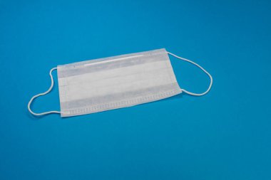 Gribe karşı korunmak için mavi renkli tıbbi maske ve mavi arka planda izole edilmiş diğer hastalıklar. Ağzı ve burnu örtmek için 3 katlı cerrahi maske. Sağlık arabası ve tıbbi konsept.
