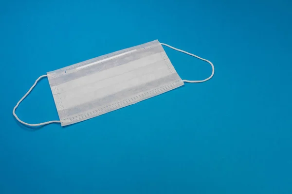 Medical mask of blue color for protection against flu and other diseases isolated on blue background. 3-ply surgical mask to cover the mouth and nose. Healthcarand medical concept.