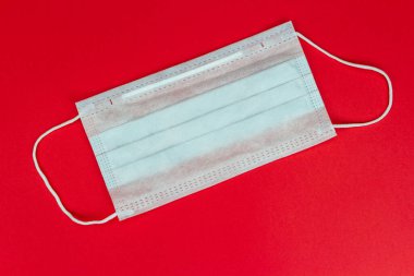 Plastik kulaklıklı cerrahi maske kırmızı arka planda virüs konsepti. Mavi yüzlü koruyucu bir maske. Bakterilerin prosedür maskesi. Koruma kavramı.