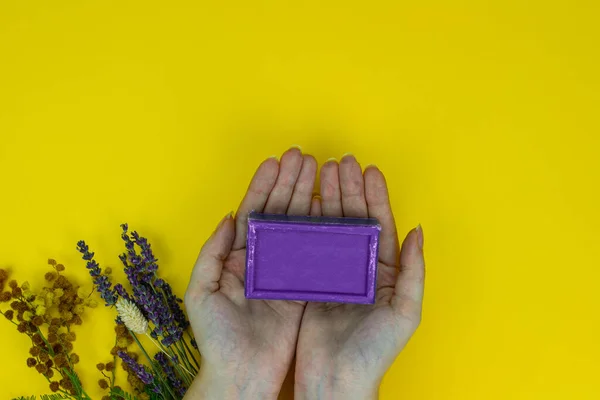 Natural Lavander soap in hands with dried aroma Lavander and flowers on the yellow background. Organic and bio concept.