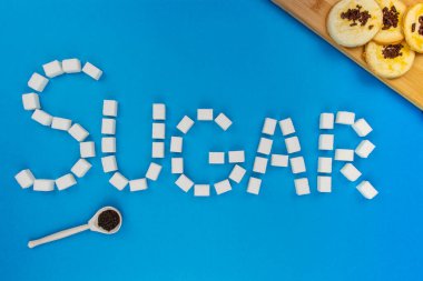 İzole edilmiş mavi bir zemin üzerinde şeker küpleri ve kurabiyeler bir kelime şeker oluşturur. Şekerden yapılmış şeker kelimelerini kavramsallaştır. Düz arkaplan.