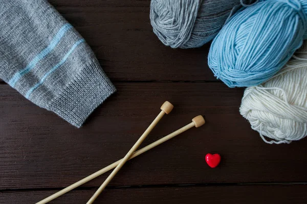 Sticka tillbehör: hylsa av stickad tröja, bollar av garn, nålar för stickning och röda hjärtat symboliserar kärlek till stickat — Stockfoto