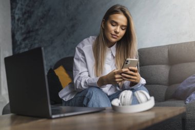 Uzun saçlı, rahat giyimli, koç koltuğunda oturan ve akıllı telefondan mesaj atan bir kız. Taşınabilir cep telefonu kullanan genç bayan.