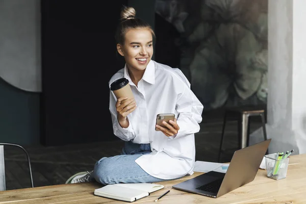 Young office worker having coffee break, relaxing at workplace, using smartphone for web chatting. Communication — Stock Photo, Image