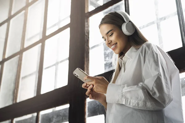 Pretty young girl in wireless headphones listening to music on smartphone. Online apps for mobile devices