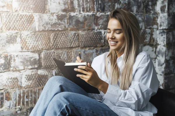 Mooie jonge zakenvrouw die op afstand van huis werkt. glimlachende vrouw zit in fauteuil op de achtergrond van een bakstenen muur — Stockfoto