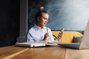Masada oturan iş kadını proje üzerinde çalışıyor. Dijital cihazları iş için kullanan genç bir kadın. Kız iletişim kuruyor