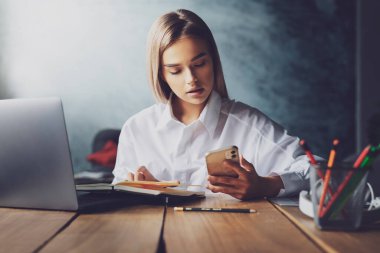Masada oturan bir kadın uzman, proje üzerinde çalışıyor. İş için bağlı dijital aygıtlar kullanan genç kadın