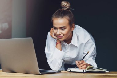 Öğrenci seminere hazırlanıyor, not defterine notlar yazıyor, internetten bilgi arıyor. Kadın çalışıyor.