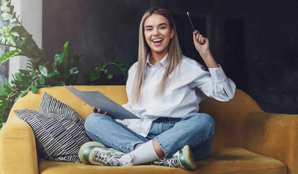 Meisje zittend op de bank, tekenend op papier met potlood. Vrolijke stemming in zelfisolatie, educatieve freelance thuisbasis — Stockfoto