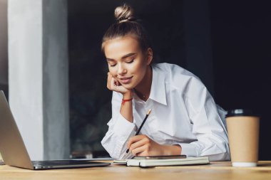 Öğrenci seminere hazırlanıyor, not defterine notlar yazıyor, internetten bilgi arıyor. Kadın çalışıyor.