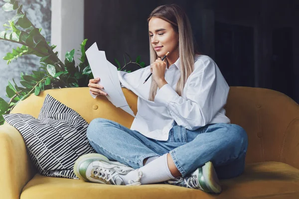 Дівчинка сидить вдома з комфортом, віддалено працюючи з документами. Жінка читає і робить нотатки з олівцем . — стокове фото