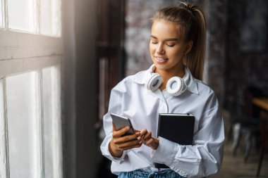 Elinde akıllı telefon ve defter tutan güzel sarışın kız. İş kadını iş için cep telefonu kullanıyor.