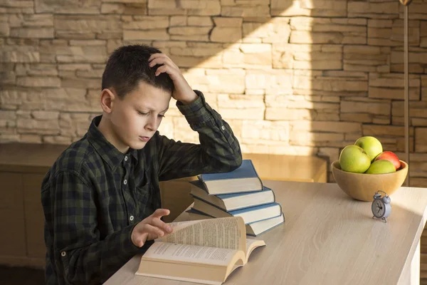 Jovem menino leitura do livro e estudando na mesa em casa — Fotografia de Stock