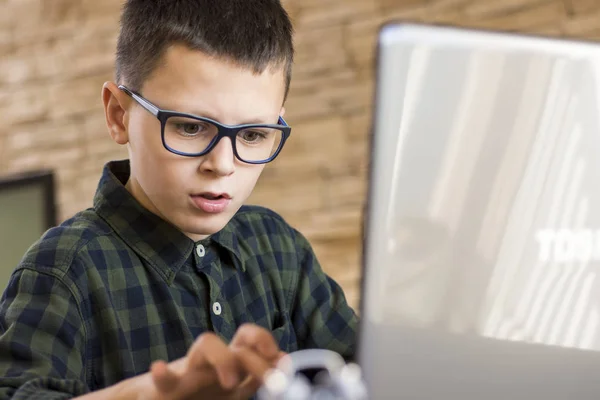 Menino com óculos usando computador portátil enquanto sentado na mesa em — Fotografia de Stock