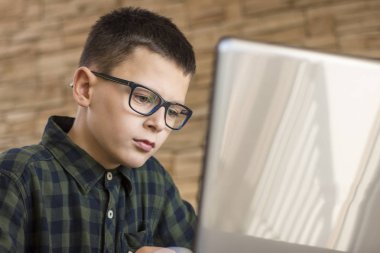 Masanın üzerinde evde otururken dizüstü bilgisayar kullanan gözlüklü çocuk. Eğitim kavramı.