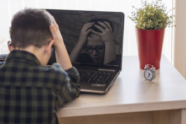 Şok çocuk masasında evde otururken dizüstü bilgisayar kullanan gözlüklü. Etkileyici yüz yansıması.