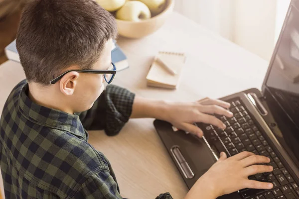 Menino com óculos usando computador portátil enquanto sentado na mesa em casa. Estudo do Conceito . — Fotografia de Stock
