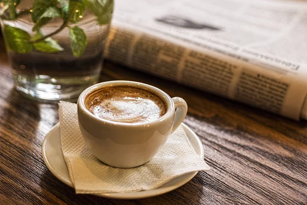 Coffee Cup, Water and Newspaper on a Wooden Table. Good Morning or Coffee Break Concept.