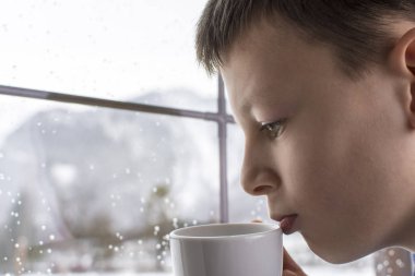 El pencere kış karlı dağ orman manzaraya bakarak çay bardağı dalgın çocukla