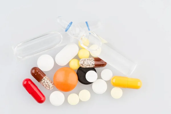 Таблетки и две ампулы на медицинском столе — стоковое фото