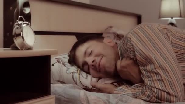 Pohledný mladý muž ležel v posteli a usmívá se otevře oči široce a skrývá pod dekou
