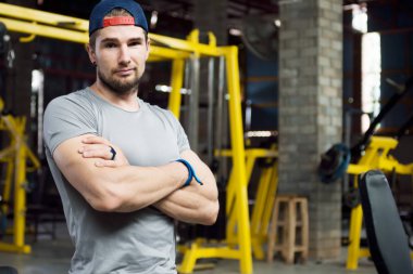Genç kas eğitmeni ayakta kol alaycı bakışla
