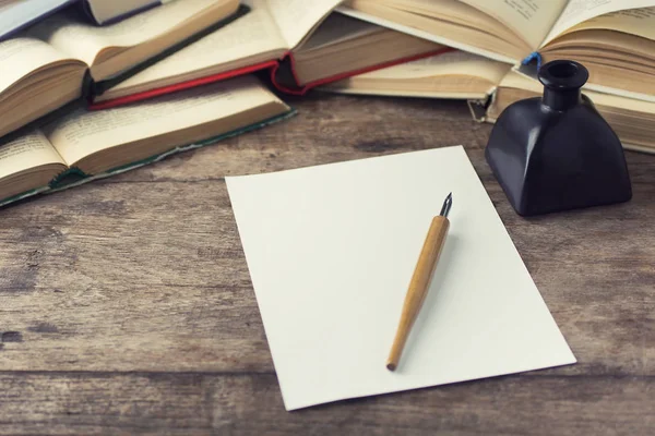 calligraphy dip pen and white paper on wooden table with books