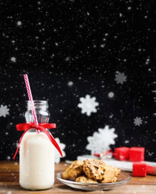 Vintage şişe süt kırmızı kurdele ve ahşap masa siyah arka plan üzerinde kar altında santas çerezler ile