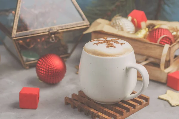 Біла чашка капучино зі сніжинкою з корицею серед різдвяних іграшок. Тло теплих фільтрованих неонових років — стокове фото
