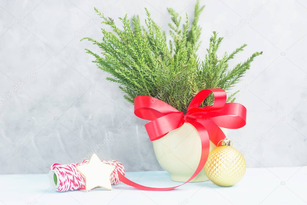 Green christmas tree branches with red bow in pot with wrapping tape and gold star against concrete grey wall. New year concept. Text space