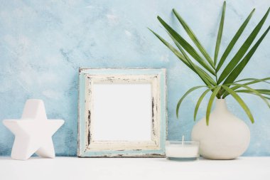 Mavi fotoğraf çerçevesi sahte vazo, seramik yıldız ve mum rafta yeşil tropikal bitki ile kare. İskandinav tarzı. Metin alanı