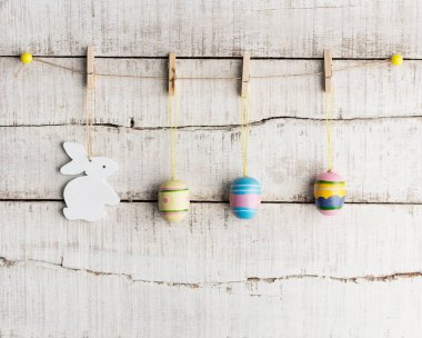 Rustik Paskalya arka plan: Vintage boyalı yumurta ve beyaz tavşan sıkı clothespins eski Beyaz ahşap duvar karşı tutun. Tatil kavramı. Metin alanı