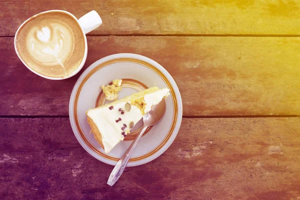 Slice of homemade pumpkin cake with cup of latte on wooden table in warm sun light. Text space